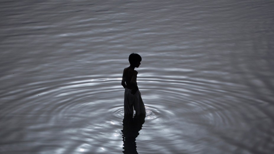 Menino toma banho em rio de Karachi, no Paquistão