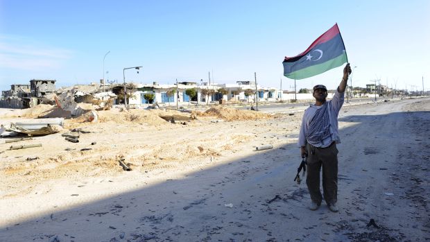Em uma Sirte destruída, rebelde comemora com bandeira líbia estiada