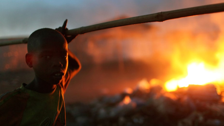 Garoto na cidade de Juba, sul do Sudão, em frente a pilha de lixo incendiado
