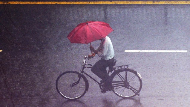 Ciclista tenta se proteger da chuva em Nova Delhi, na Índia
