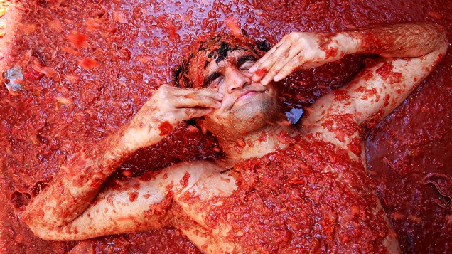 Folião nada em molho de tomate na vila espanhola. Cem toneladas de tomate foram usadas em uma das maiores guerras de comida do mundo, que se encontra em sua 64ª edição