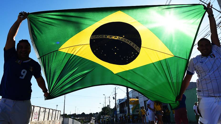 Torcedores seguram a bandeira do Brasil em frente à Arena Amazônia antes do jogo entre Inglaterra e Itália, em Manaus