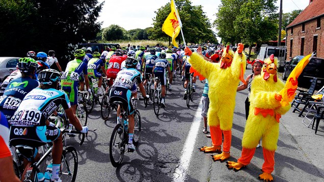 Ciclistas passam por espectadores vestindo com trajes de frango durante a segunda etapa da Volta da França