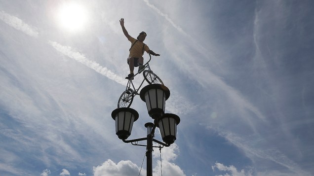 Artista se equilibra em cima de sua bicicleta num poste de luz antes da 11.ª etapa ‎da volta da França