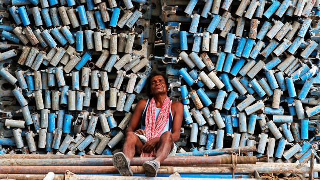Trabalhador tira um cochilo ao lado de uma pilha de tubos de ferro em uma construção de um complexo comercial na cidade indiana de Chennai