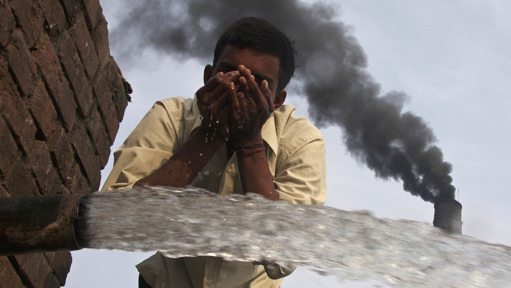Trabalhador indiano bebe água de uma bica em fábrica de tijolos da vila de Togga, em Chandigarh, norte do país