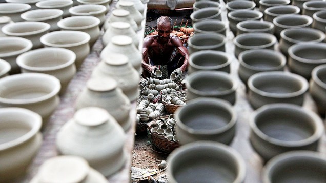Oleiro coloca potes de barro em uma cesta para secar, dentro de uma oficina em Kolkata, na Índia