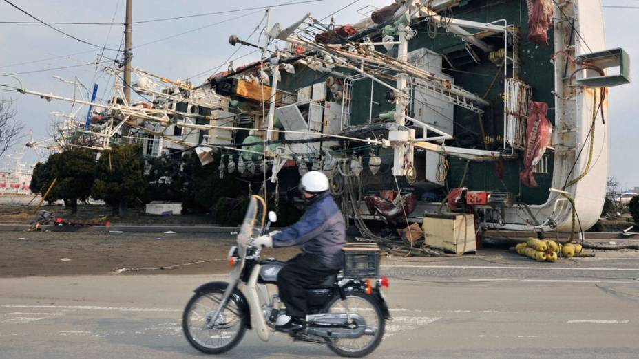 Homem passa de motocicleta próximo a barco arrastado pelo tsunami