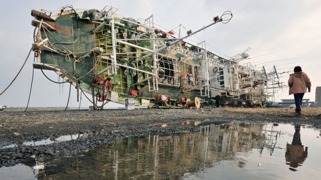 Japonês passa por restos de barco arrastado por tsunami na cidade de Hachinohe, no Japão