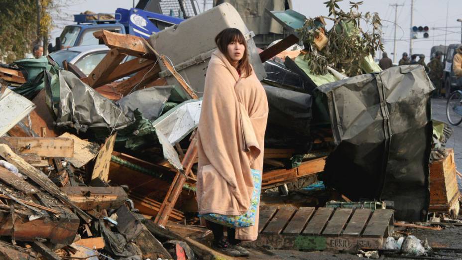 Japonesa observa restos das casas da cidade de Ishimaki, após terremoto e tsunami ter atingido a cidade