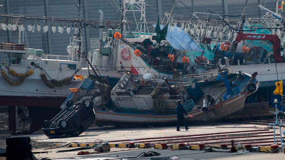 Oficial caminha entre barcos e carros arrastados pelo tsunami que atingiu a cidade de Hachinohe, no Japão