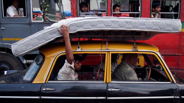 Homem segura colchão transportado no teto de um táxi em Mumbai, na Índia