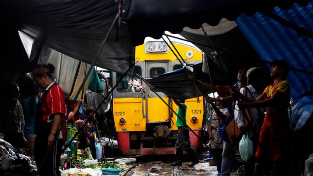 Feirantes retiram frutas e toldos para trem passar em Maeklong, na Tailândia. A feira precisa ser desmontada oito vezes ao dia para a passagem dos vagões