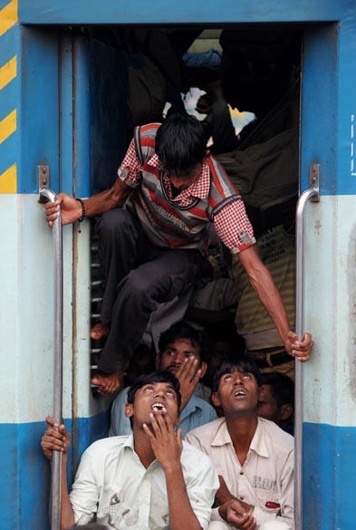 Passageiro escala a porta para sair do trem em estação de Nova Délhi, na Índia