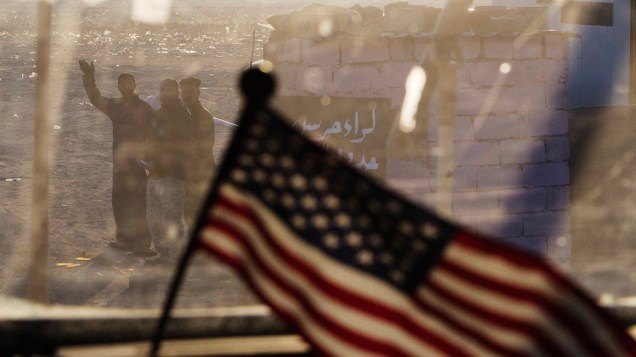 Iraquianos acenam para veículo das tropas americanas, durante o embarque dos últimos militares para os Estados Unidos - 18/12/2011