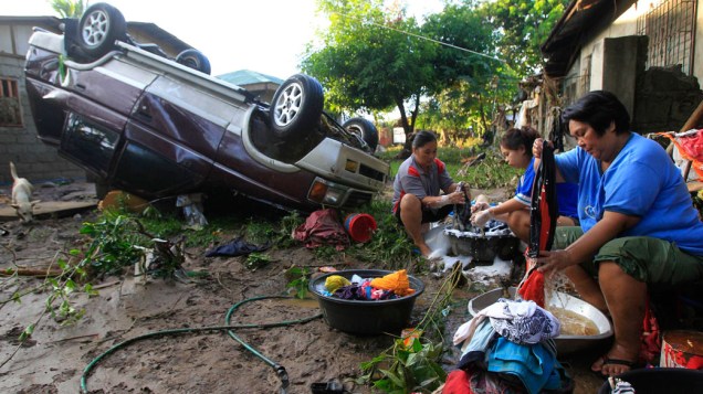 Mulheres lavam roupas ao lado de carro atingido por tufão, em Cagayan de Oro, nas Filipinas - 18/12/2011