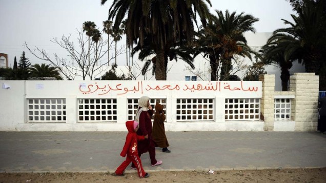 Família caminha em frente as marcas deixadas pelos protestos em Tunis