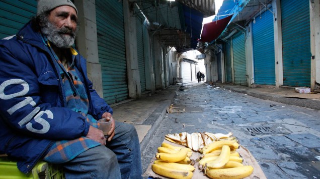 Vendedor de bananas senta ao lado de lojas fechadas em Tunis, na Tunísia durante os protestos contra o governo que já dura 23 anos - 13/01/2011
