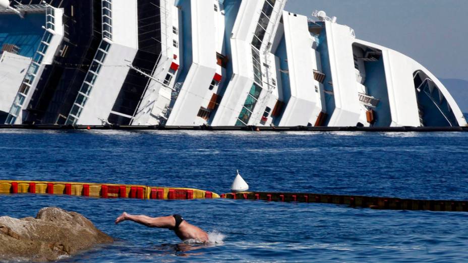 Turistas desfrutam praia, próximo do navio Costa Concordia que naufragou, na Espanha