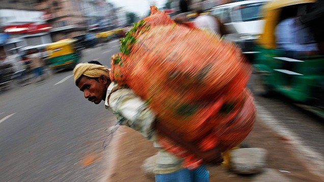 Trabalhador carrega um saco de verduras e espera para atravessar a rua, em Nova Deli, na Índia