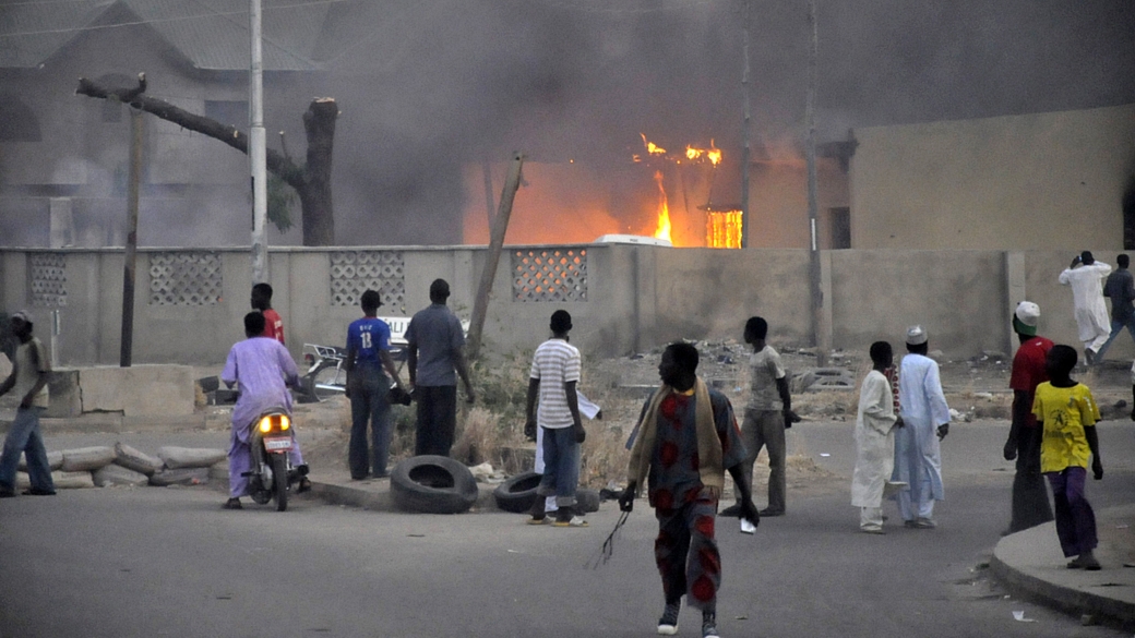 Moradores de Kano, a segunda maior cidade da Nigéria, observam as chamas em delegacia que foi alvo de ataques
