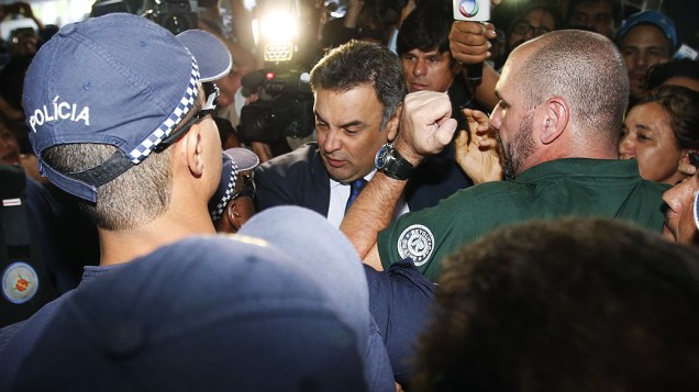 O senador Aécio Neves (PSDB-MG) chega ao Congresso Nacional, em Brasília, passando por manifestantes contrários à aprovação da alteração da meta fiscal