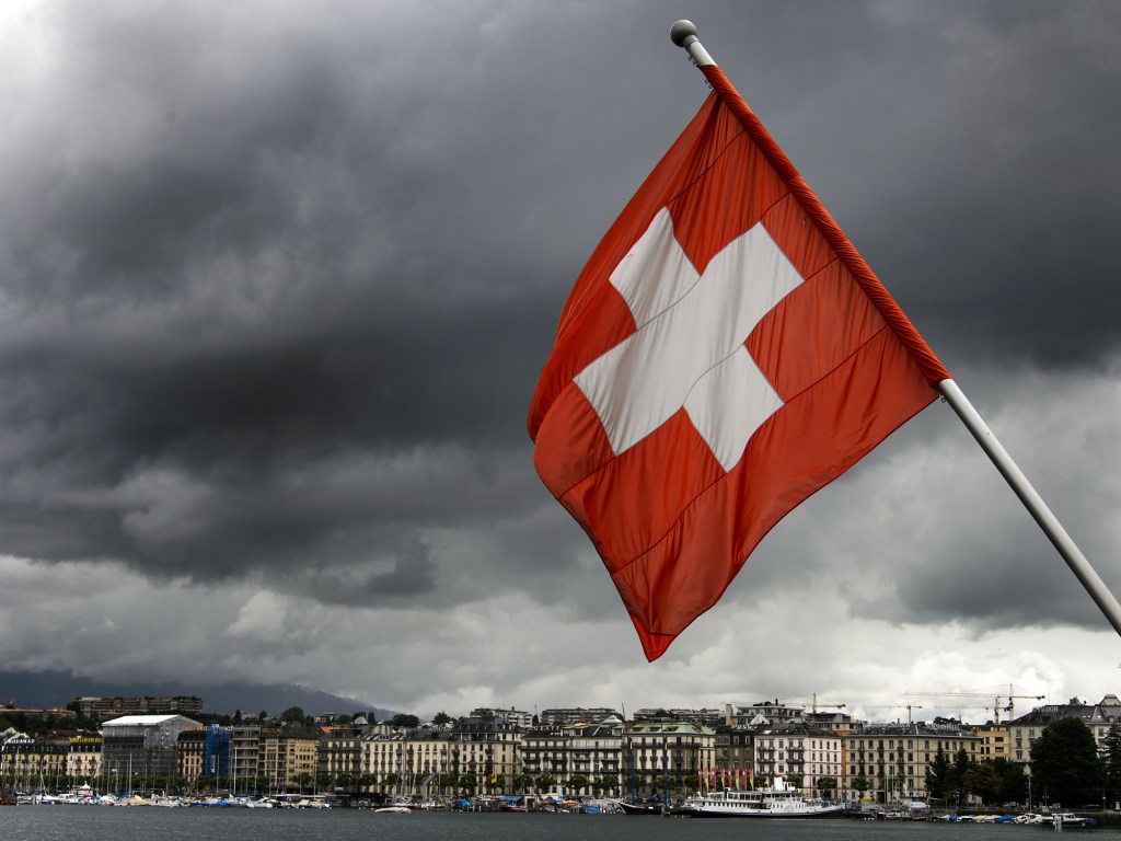 Bandeira da Suíça tremula com rio Geneva atrás