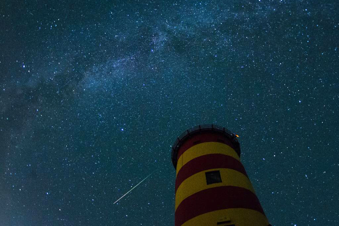 Uma estrela cadente cruza o céu atrás do farol em Pilsum, noroeste da Alemanha, durante o pico da atividade da chuva anual de meteoros Perseidas - 13/08/2015