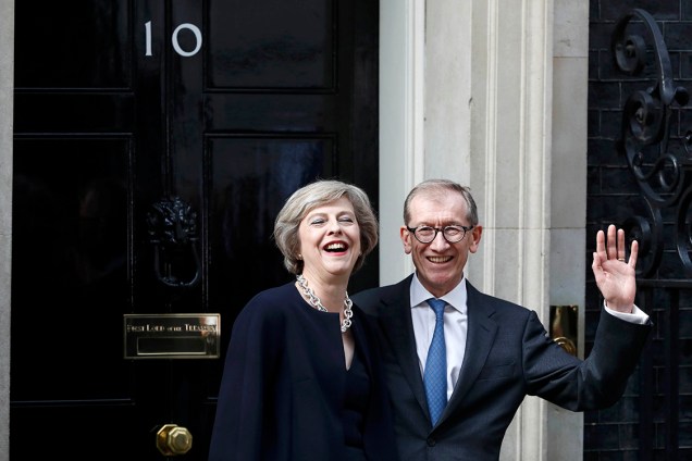 Theresa May, nomeada Primeira-Ministra da Inglaterra, acena para fotógrafos ao lado do marido, Phillip, em frente ao gabinete que ocupará durante seu mandato - 13/07/2016