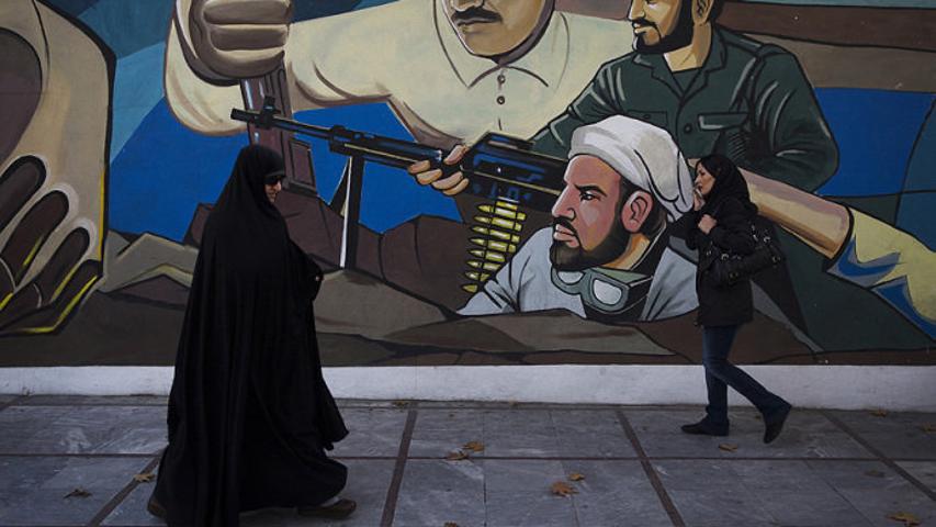 Mulher caminha diante de mural que celebra a revolução iraniana