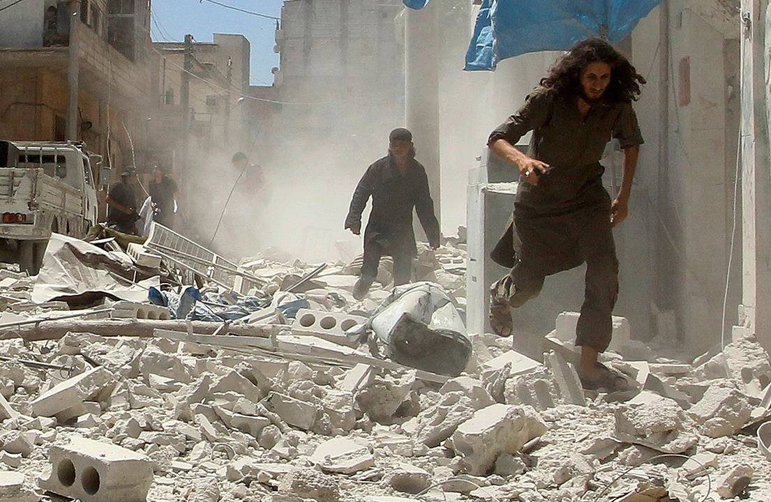 Homens correm por entre escombros e prédios destruídos por um ataque aéreo na cidade de Idlib, Síria