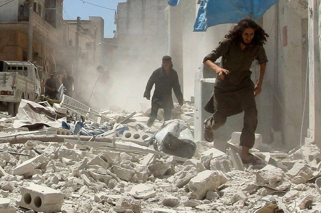 Homens correm por entre escombros e prédios destruídos por um ataque aéreo na cidade de Idlib, Síria