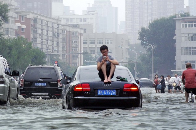 Homem senta-se em cima de um carro enquanto fica preso em uma rua inundada em Tianjin, na China