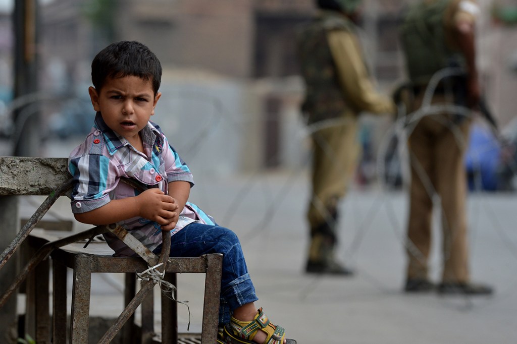 Garoto da região da Caxemira observa movimento na rua enquanto guardas paramilitares realizam toque de recolher pelo 17° dia seguido em Srinagar, na Índia
