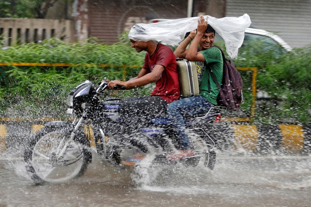 Jovens se protegem da chuva com um saco plástico na cabeça enquanto dirigem uma motocicleta pelas ruas de Ahmedabad, na Índia - 27/07/2016