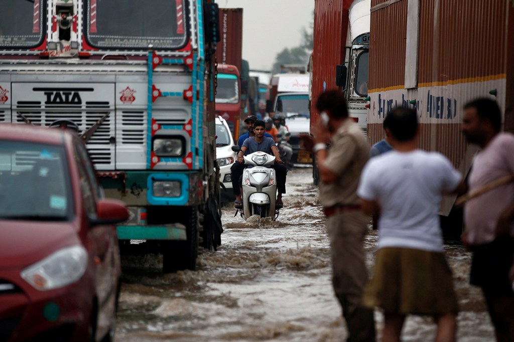 Veículos tentam passar por regiões alagadas após fortes tempestades atingirem a região de Gurugram, nos arredores de Nova Délhi, Índia