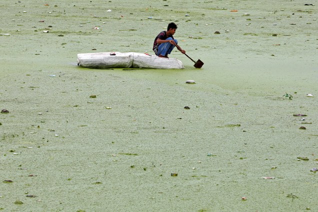 Garoto rema em uma balsa improvisada pelo rio Sabarmati, coberto por algas, na cidade de Ahmedabad, Índia - 27/07/2016