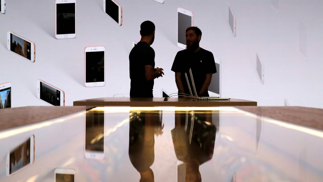 Vendedores conversar em frente a uma tela com iPhones expostos durante evento da Apple Store de Williamsburg, no Brooklyn, Nova York