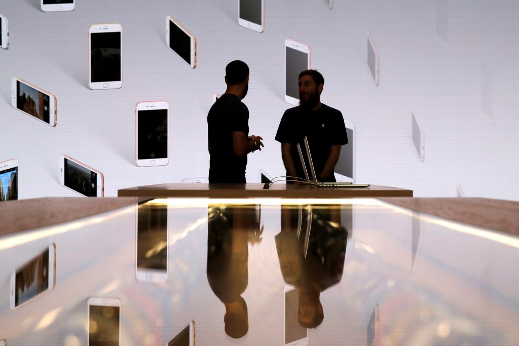 Vendedores conversar em frente a uma tela com iPhones expostos durante evento da Apple Store de Williamsburg, no Brooklyn, Nova York