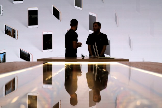 Vendedores conversar em frente a uma tela com iPhones expostos durante evento da Apple Store de Williamsburg, no Brooklyn, Nova York - 28/07/2016