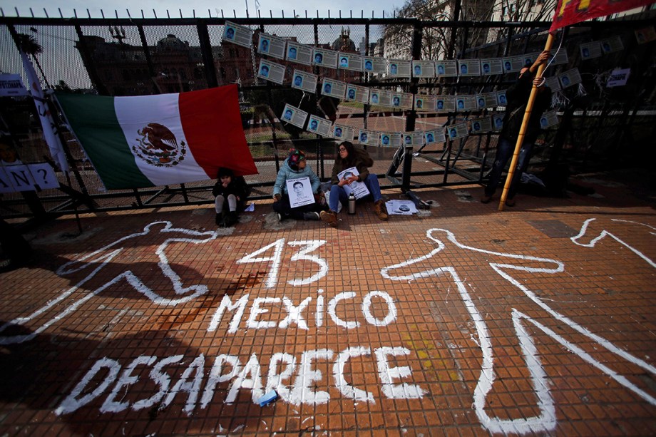 Manifestantes sentam ao lado de grafite desenhado no chão em protesto à visita do presidente do México, Enrique Pena Nieto, à Argentina, na cidade de Buenos Aires, por causa do desaparecimento dos estudantes da Universidade de Ayotzinapa - 29/07/2016