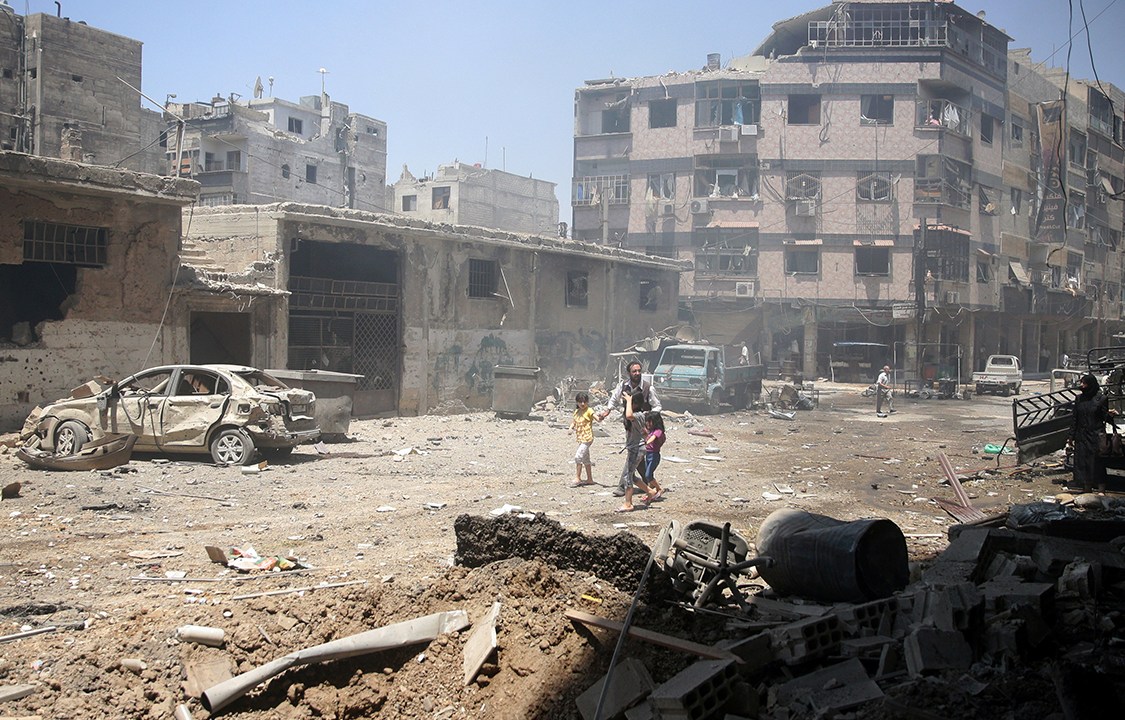 Civis caminham por entre escombros após ataque aéreos que atingiram a região de Damasco, na Síria