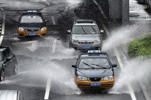 Automóveis andam no meio de rua inundada, em Pequim, na China, após fortes chuvas atingirem a região - 20/07/2016