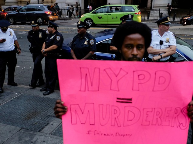 Homem segura um cartaz escrito "Policia de Nova York assassinos"