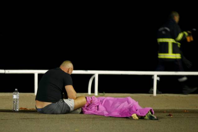 Homem fica sentado ao lado de um corpo no local do ataque durante as celebrações do Dia da Bastilha em Nice, na França - 14/07/2016