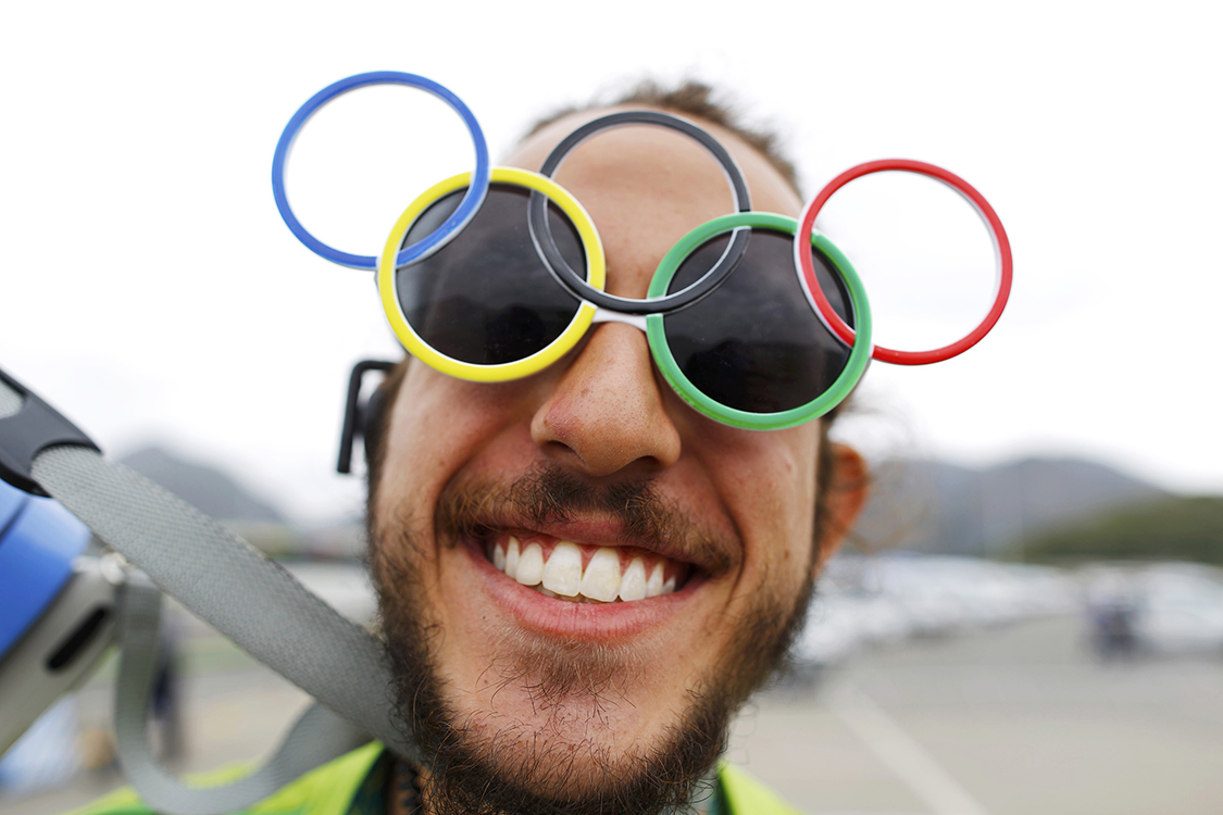 Voluntário usa óculos com símbolo das Olímpiadas, os aros interligados, na Vila Olímpica, Rio de Janeiro