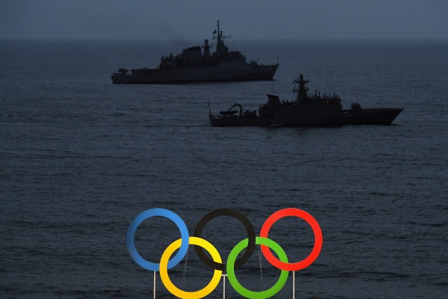 Navios de guerra são vistos por trás dos anéis olímpicos a partir da Arena do Vôlei de Praia na praia de Copacabana