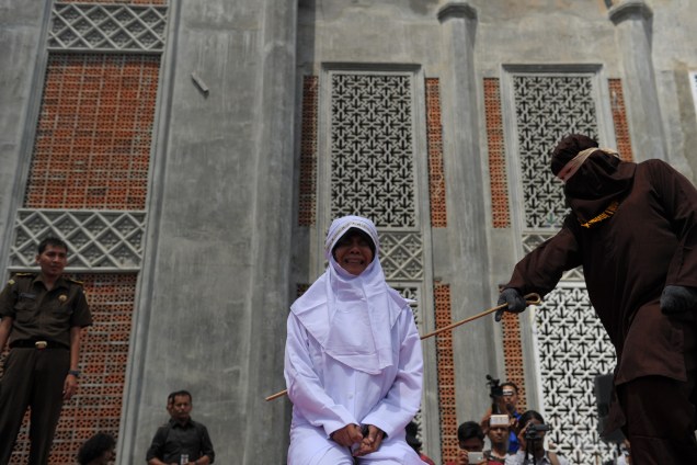 Mulher é castigada com golpes de bastão como punição por encontrar um homem sem estar casada com ele, atitude condenada pela lei islâmica da Sharia, em frente a uma mesquita em Banda Aceh, na Indonésia - 01/08/2016