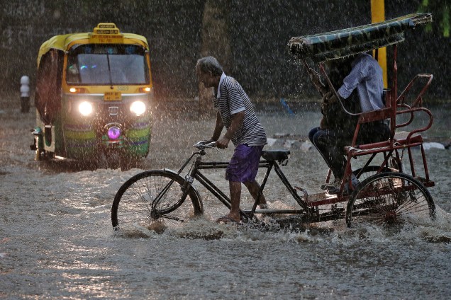 Homem transporta passageiros em sua bicicleta em meio a uma rua inundada em Nova Délhi, na Índia - 31/08/2016