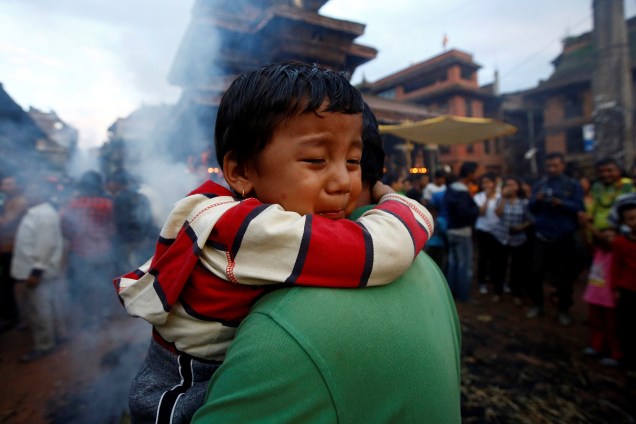 Criança abraça a mãe, enquanto pessoas colocam fogo em uma efígie que representa o demônio Ghantakarna para simbolizar a destruição do mal durante um festival na cidade de Bhaktapur, no Nepal